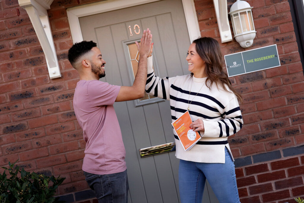 Young couple doing a high five outside the front door of their new home