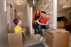 Young family in the hallway of their new home, cheeky son hiding in a moving box